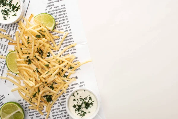 Vue du haut des frites croustillantes, sauce à l'ail et citron vert tranché sur papier journal blanc — Photo de stock