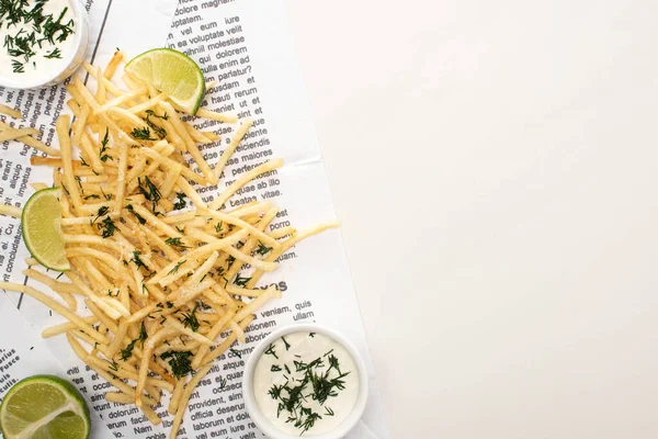 Top view of crispy french fries, garlic sauce and sliced lime on newspaper on white — Stock Photo