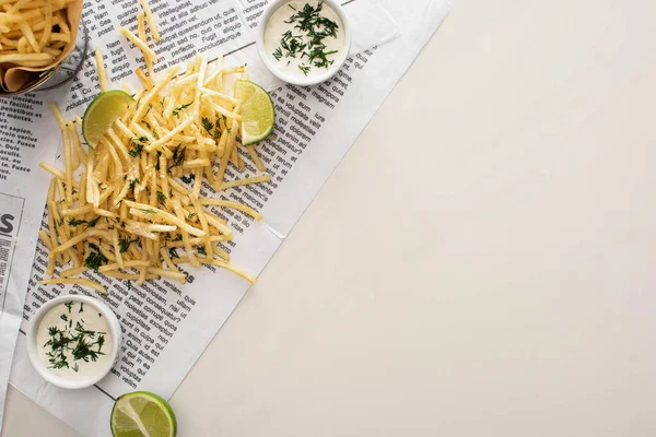 Vista superior de batatas fritas salgadas, molho de alho e limão fatiado no jornal em branco — Fotografia de Stock