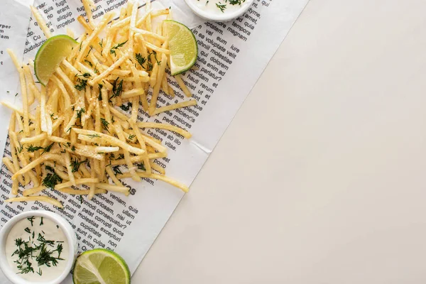 Vue du dessus des frites frites, de la sauce à l'ail et du citron vert tranché sur papier journal blanc — Photo de stock