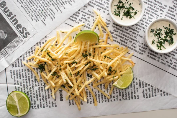 Vue du dessus des frites frites, de la sauce à l'ail et du citron vert tranché sur le journal — Photo de stock