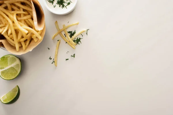 Vista superior de papas fritas crujientes, salsa de ajo y lima en rodajas sobre blanco - foto de stock