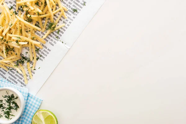 Vue du dessus des frites, de la sauce à l'ail et de la lime tranchée sur papier journal blanc — Photo de stock