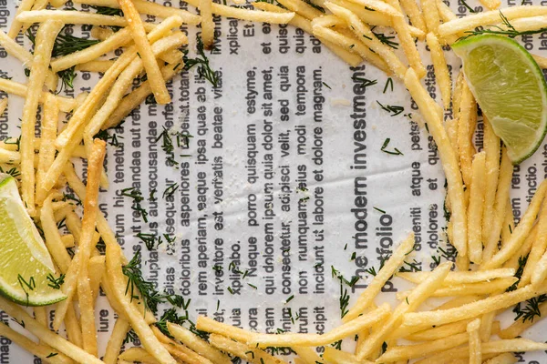 Top view of crispy french fries, sliced lime and dill on newspaper — Stock Photo