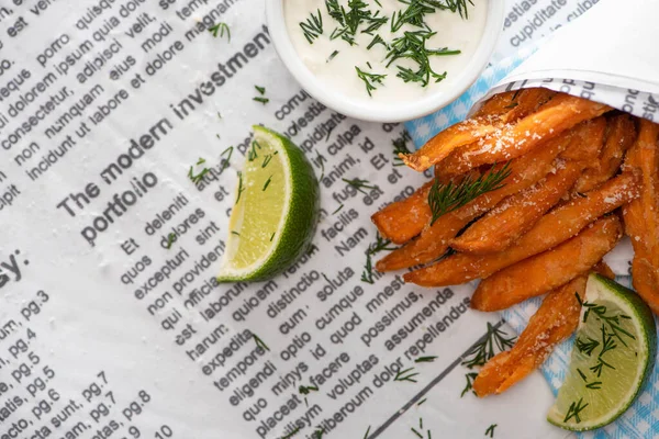 Vista superior de papas fritas crujientes, lima en rodajas y salsa de ajo en el periódico - foto de stock