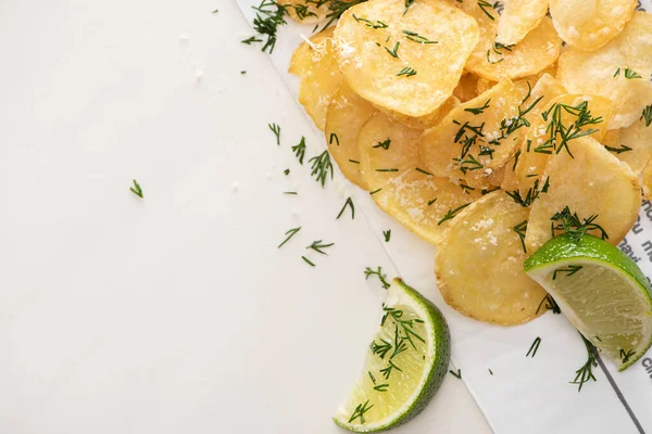 Top view of crunchy potato chips with salt near sliced lime on white — Stock Photo