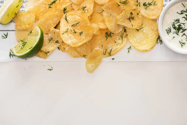 Top view of crunchy potato chips with salt near sliced lime and garlic sauce on white — Stock Photo