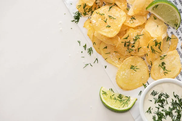 Вид сверху на картофельные чипсы с солью рядом с нарезанной известью и чесночным соусом на белом — стоковое фото