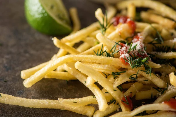 Close up of tasty french fries with ketchup, salt and dill near sliced lime — Stock Photo