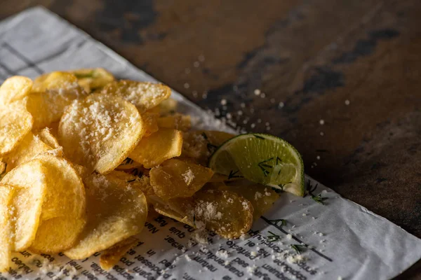 Selective focus of crunchy potato chips with salt near sliced lime and newspaper on marble surface — Stock Photo