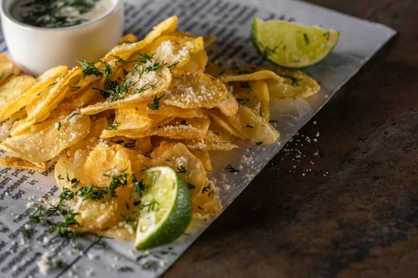 Selective focus of potato chips with salt near sliced lime, garlic sauce and newspaper on marble surface — Stock Photo