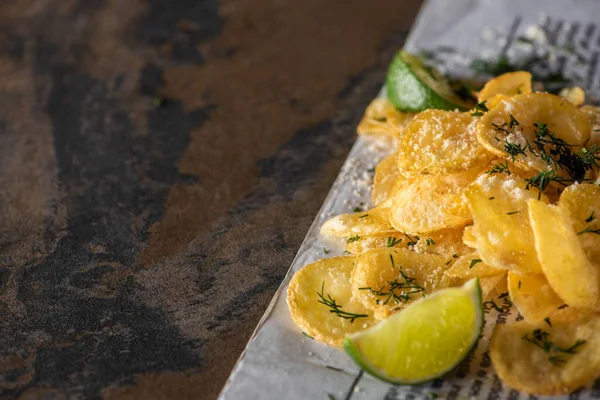 Selective focus of salty potato chips near sliced lime and newspaper on marble surface — Stock Photo