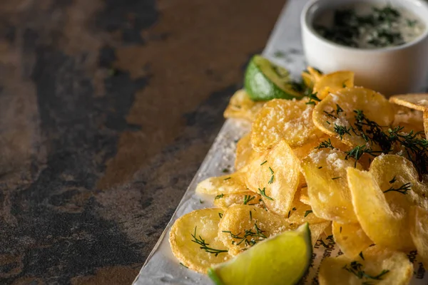 Enfoque selectivo de papas fritas saladas cerca de lima en rodajas, salsa de ajo y periódico en la superficie de mármol - foto de stock