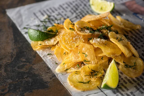 Selective focus of potato chips near sliced lime and newspaper on marble surface — Stock Photo