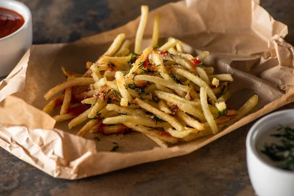 Saborosas batatas fritas em papel manteiga perto de ketchup e molho de alho na superfície de mármore — Fotografia de Stock