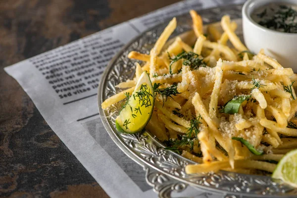 Fuoco selettivo di patatine fritte, salsa all'aglio e lime affettato sul giornale — Foto stock