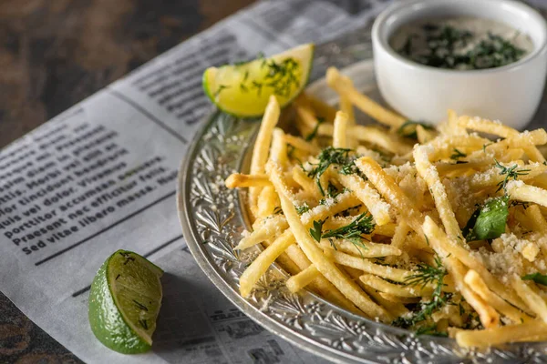 Fuoco selettivo di patatine fritte salate, salsa all'aglio e lime affettato vicino al giornale — Foto stock