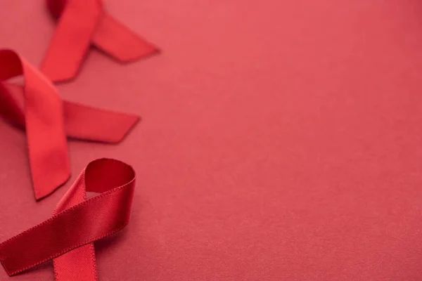 Selective focus of red awareness aids ribbons on red background with copy space — Stock Photo
