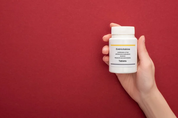 Cropped view woman holding of container with emtricitabine tablets on red background — Stock Photo