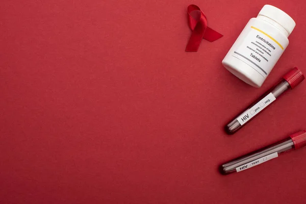 Vue du dessus du ruban rouge des aides de sensibilisation, des pilules d'emtricitabine et des éprouvettes avec des échantillons de sang sur fond rouge — Photo de stock