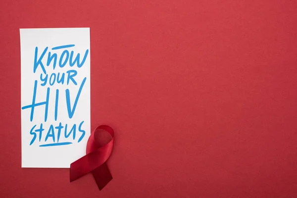 Vista dall'alto della scheda con conoscere il tuo stato HIV lettering e nastro di consapevolezza su sfondo rosso — Foto stock