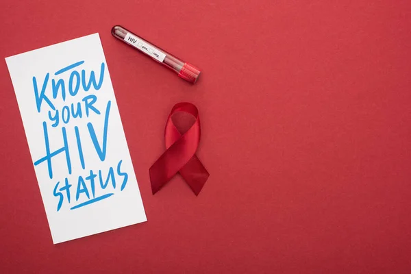 Top view of card with know your HIV status lettering and awareness ribbon with blood sample on red background — Stock Photo