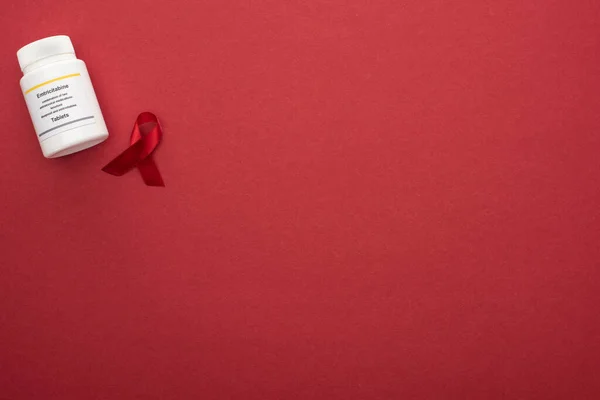 Top view of red awareness aids ribbon and emtricitabine tablets on red background — Stock Photo