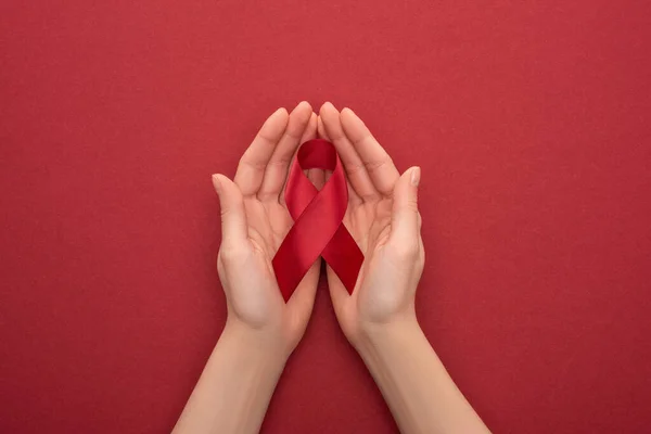 Cropped view of woman holding red awareness aids ribbon on red background — Stock Photo