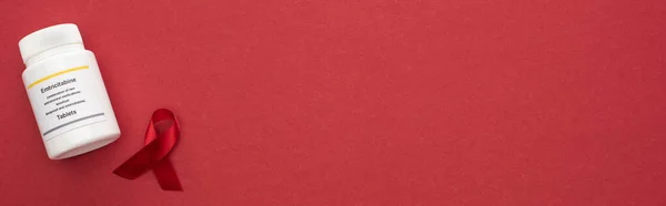 Top view of red awareness aids ribbon and emtricitabine tablets on red background, panoramic shot — Stock Photo