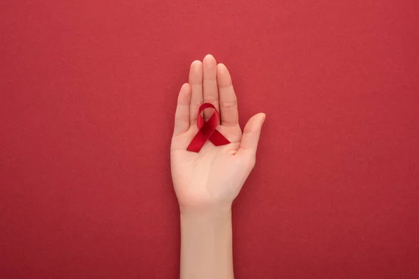 Vista recortada de la mujer que sostiene la cinta roja de las ayudas de la conciencia sobre fondo rojo - foto de stock