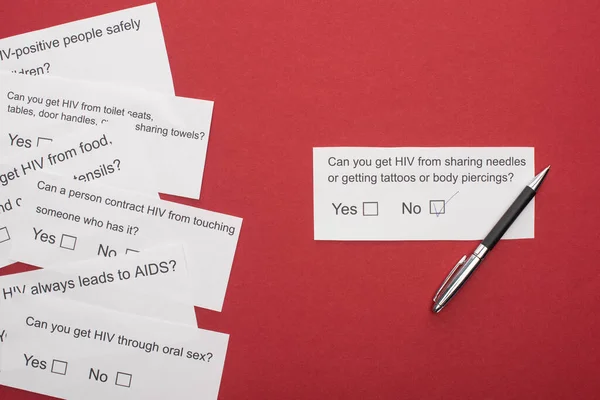 Top view of paper cards with HIV questionnaire and pen on red background — Stock Photo