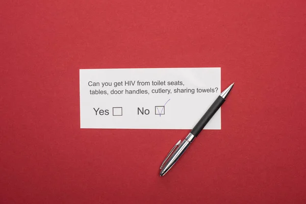 Top view of paper card with HIV questionnaire and pen on red background — Stock Photo