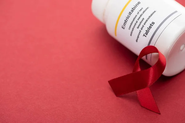 Красная осведомленность помогает ленту и контейнер с эмбриитабином таблетки на красном фоне — стоковое фото