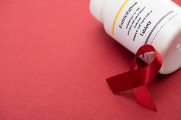 Red awareness aids ribbon and container with emtricitabine tablets on red background — Stock Photo