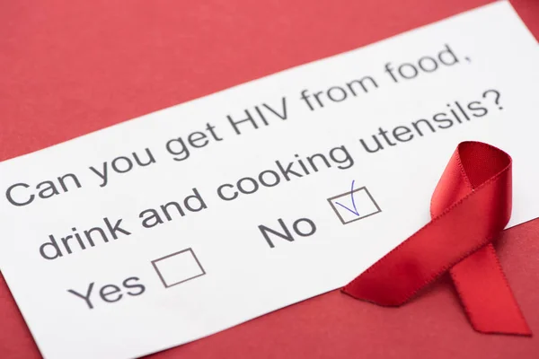 Tarjeta de papel con cuestionario sobre VIH con cinta de sensibilización sobre fondo rojo - foto de stock