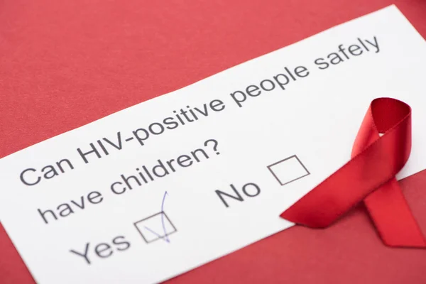 Paper card with HIV questionnaire with awareness ribbon on red background — Stock Photo