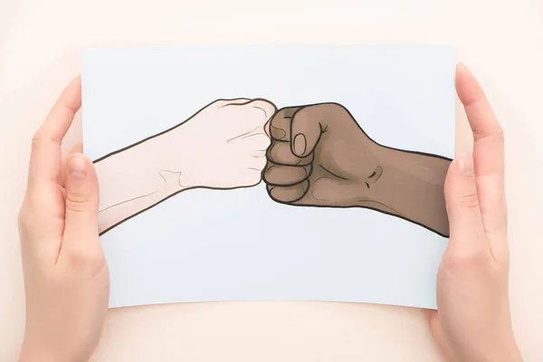 Vista recortada de la mujer sosteniendo la imagen con las manos multiétnicas dibujadas haciendo golpe de puño sobre fondo beige - foto de stock