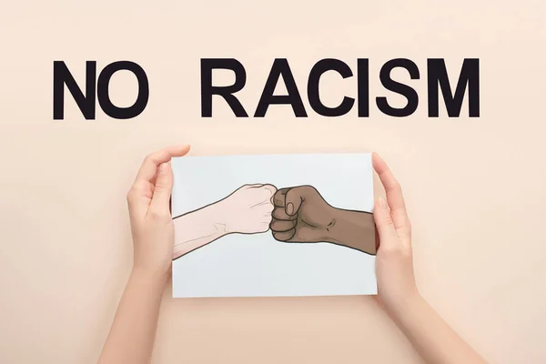 Vista recortada de la mujer sosteniendo la imagen con las manos multiétnicas dibujadas haciendo golpe de puño casi sin letras de racismo sobre fondo beige - foto de stock