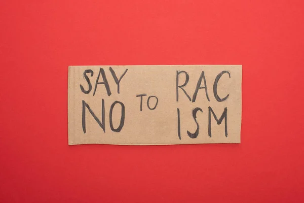 Vista superior del cartel de cartón con decir no a las letras racistas sobre fondo rojo - foto de stock