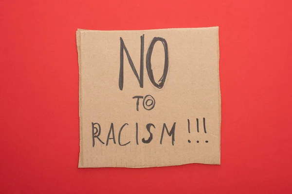 Vista superior del cartel de cartón con letras no al racismo sobre fondo rojo - foto de stock