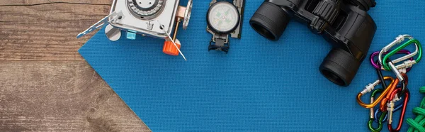 Panoramic shot of gas burner, compass, binoculars and carabiners on blue sleeping pad on wooden surface — Stock Photo