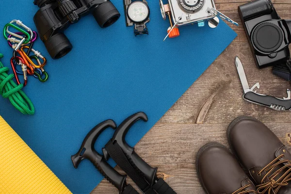 Vista superior do equipamento de caminhadas no tapete de dormir azul, câmera fotográfica e botas na mesa de madeira — Fotografia de Stock