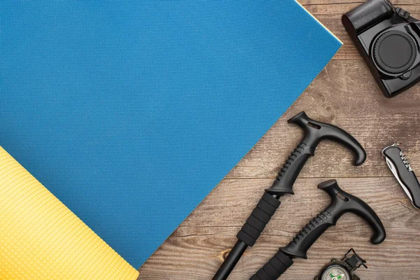 Top view of blue sleeping mat, trekking poles, photo camera, jackknife and compass on wooden table — Stock Photo