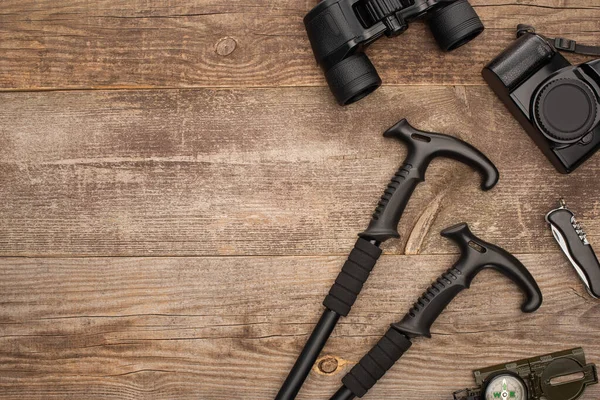 Top view of trekking poles, binoculars, photo camera, compass and jackknife on wooden surface — Stock Photo