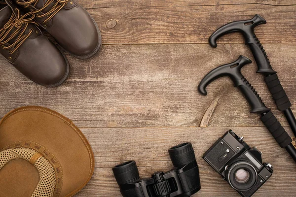 Vista superior de botas, chapéu, binóculos, câmera fotográfica e postes de trekking na superfície de madeira — Fotografia de Stock