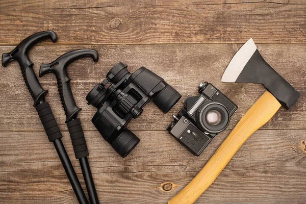 Vista dall'alto di bastoncini da trekking, binocolo, macchina fotografica e ascia su superficie in legno — Foto stock