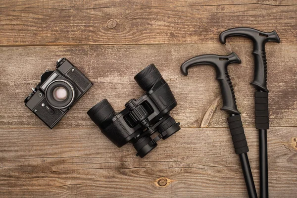 Top view of photo camera, binoculars and trekking poles on wooden table — Stock Photo