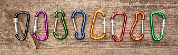 Panoramic shot of colorful carabiners on wooden table — Stock Photo