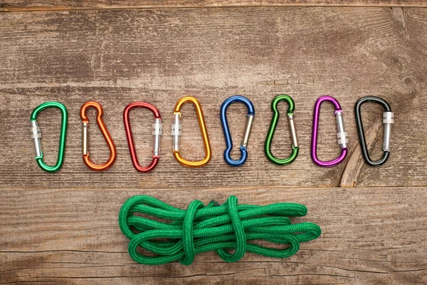 Top view of colorful carabiners and green hiking rope on wooden table — Stock Photo