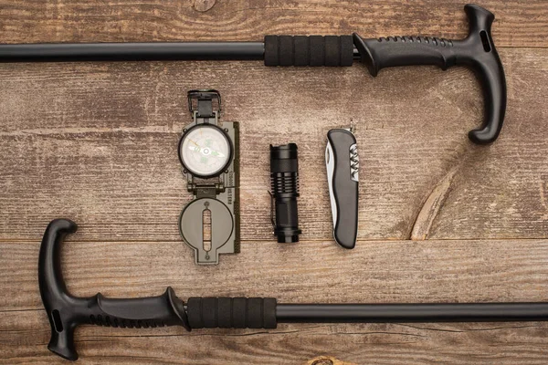 Ansicht von Trekkingstöcken, Kompass, Taschenlampe und Mantelmesser auf Holztisch — Stockfoto